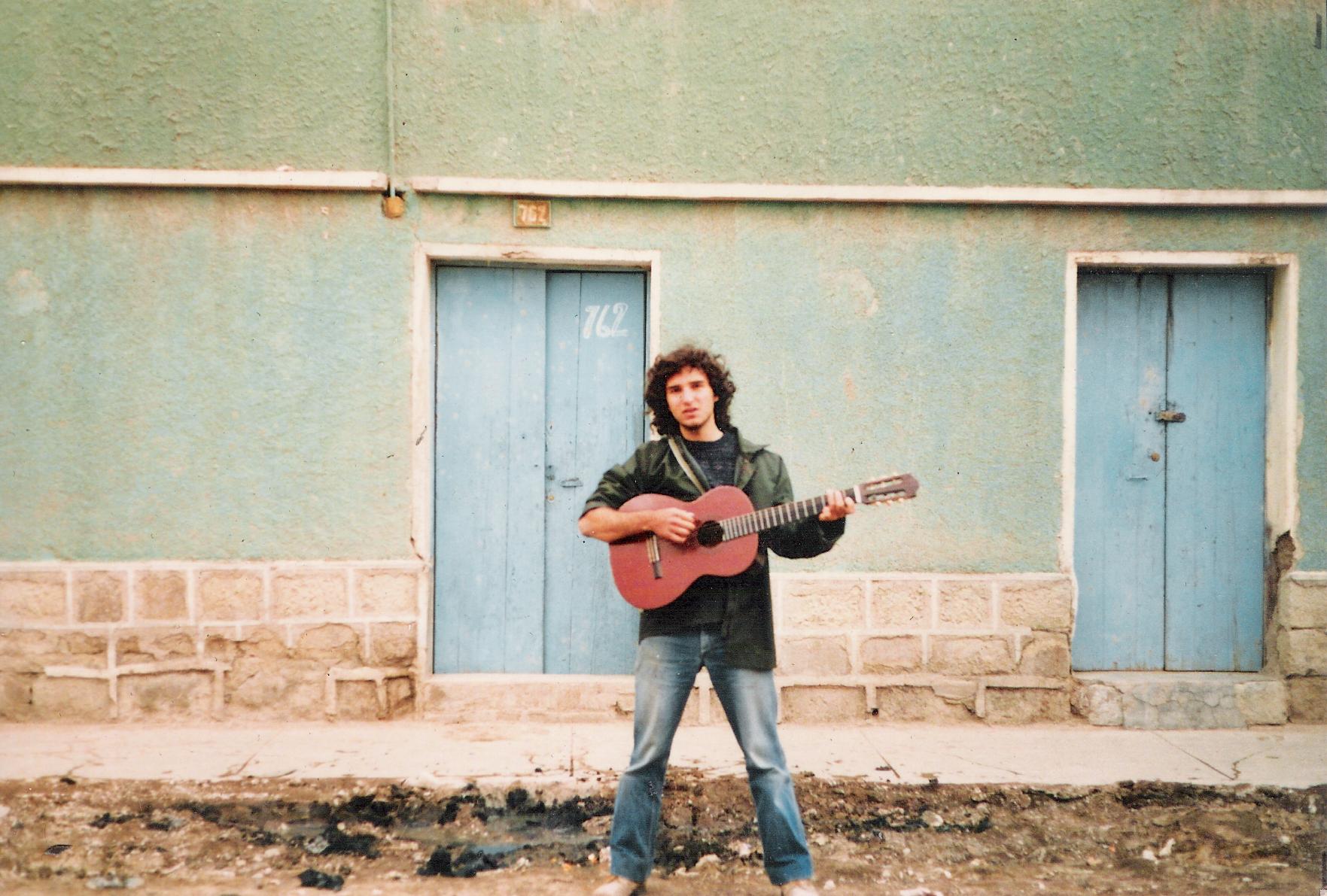 Photo of Nedjo playing a guitar in front of a row of houses.
